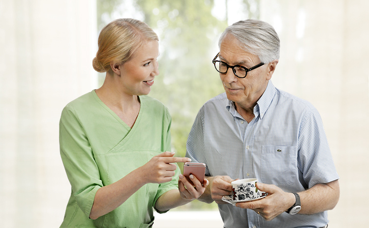 Elderly man looking at smart phone with a nurse.